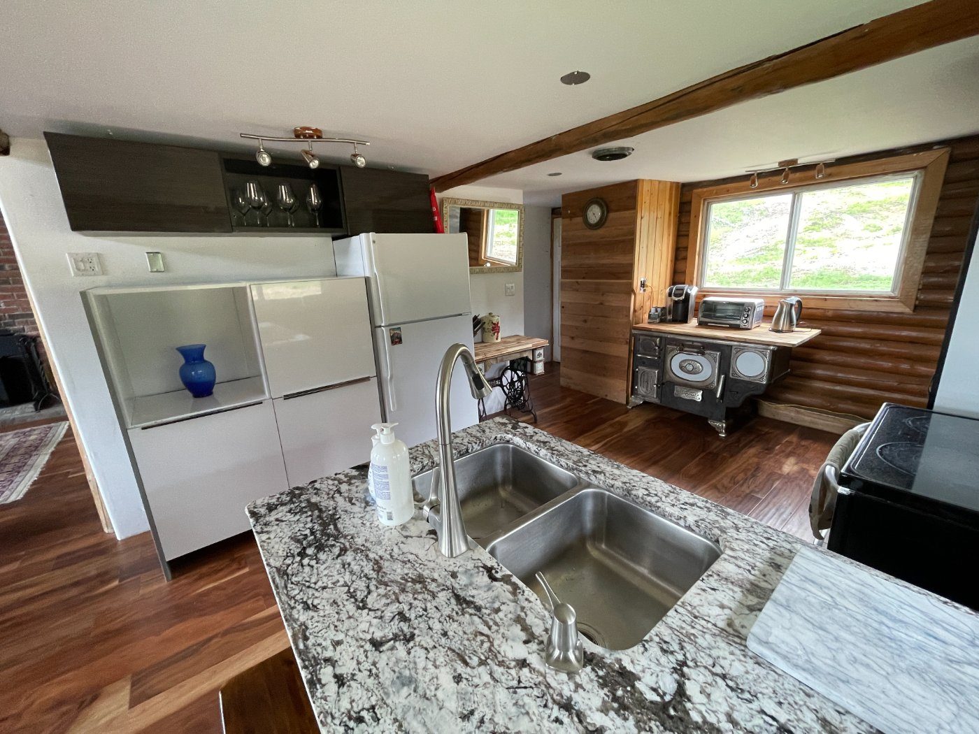 The kitchen island with double sink, granite counter, white cabinetry and antique cookstove beyond