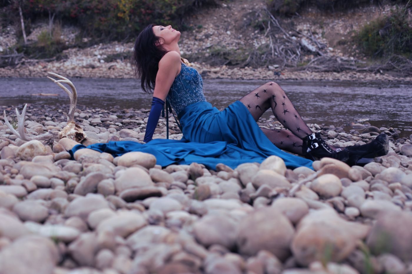 Samia by the river at dusk, in a blue gown among the stones