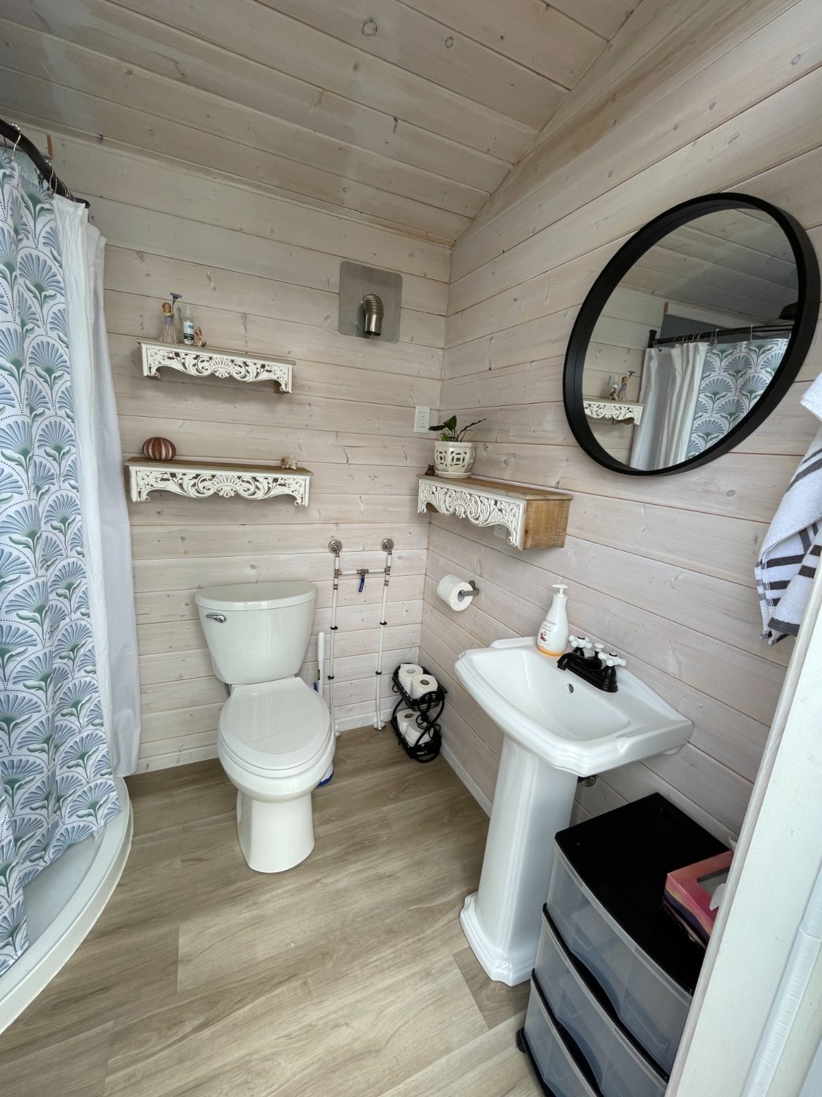 Inside the washhouse—pedestal sink, round mirror, shower and shiplap walls